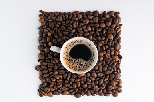 Coffee cup surrounded by roasted beans on white surface