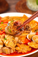 Octopus tentacles with chopsticks over seafood stew with clams and mixed vegetables in traditional Asian cuisine
