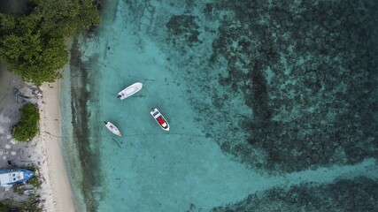 Aerial view of boats resting on turquoise waters near a white sandy beach contrasting with the lush greenery of the shore, Maldives, Maldives.