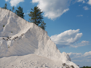 Beautiful white mountain with chalk deposit with resilient green pine trees against blue sky and...