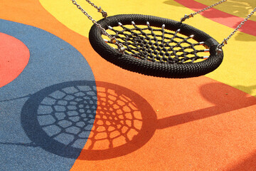A black spider web swing in colorful playground. Resemble bird nest in shape and able to carry multiple people. One of popular play installation at children's playground.
