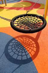 A black spider web swing in colorful playground. Resemble bird nest in shape and able to carry multiple people. One of popular play installation at children's playground.