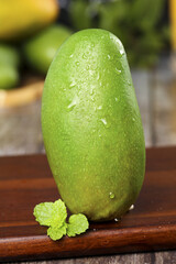 Fresh Green Mango with Water Droplets on Wooden Board with Mint Garnish