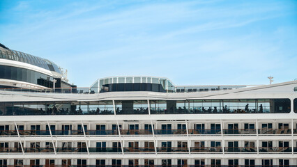 Obraz premium Detailed view of a modern cruise ship - section with balcony cabins, lounge area, and silhouettes of passengers against a blue sky.