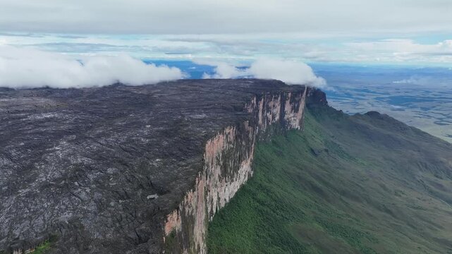 Aerial view of Mount Roraima where dark rocky plateau contrasts with lush green slopes beneath its towering cliffs, Paraitepui, Canaima, Venezuela.
