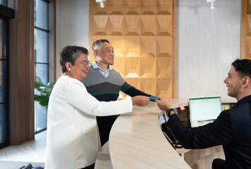 Senior asian couple interact with a hotel receptionist while checking in to their room. The...