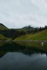 Misty Alpine Lake and Verdant Mountains under a Cloudy Sky, featuring a tranquil reflection and a...