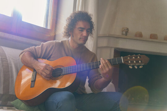 Man playing acoustic guitar at home with sunlight