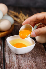 Farm Fresh Eggs with Bright Orange Yolks Being Cracked into Bowl on Rustic Wooden Background