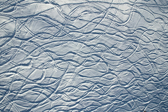 Aerial view of snowy expanse crisscrossed with rhythmic ski tracks, carving elegant curves across the pristine white canvas, Frais, Piemonte, Italy.