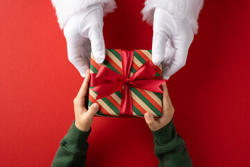A child receiving a wrapped gift box with red ribbon from Santa Claus hands, festive scene