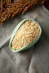 Sorghum grain in bowl with wheat spikes - healthy whole grain cereal crop on rustic background