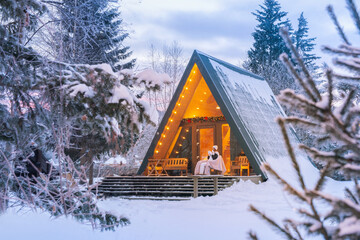 warm drink on the porch of an A-frame cabin in a serene winter forest during the early morning...