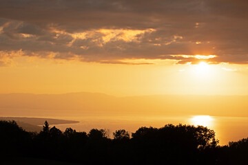 Coucher de soleil sur le lac Léman or brillant dans un ciel de nuages sombres avec vue sur sur la silhouette de la rive suisse. 