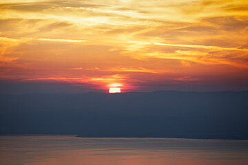 Coucher de soleil sur le lac Léman or brillant dans un ciel de nuages en feu rouge et jaune avec vue sur sur la silhouette de la rive suisse. 