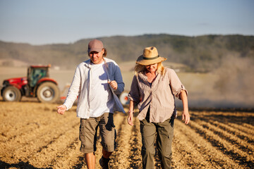 Man and woman farmers discussing agricultural activity as tractor works on field during sowing season. Teamwork in agriculture