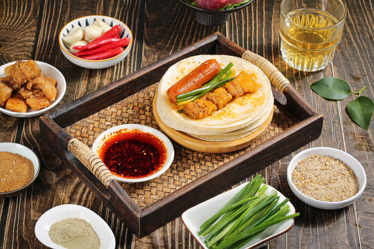 Chinese Grilled Meat Pancakes with Spicy Sauce and Traditional Accompaniments on Wooden Table
