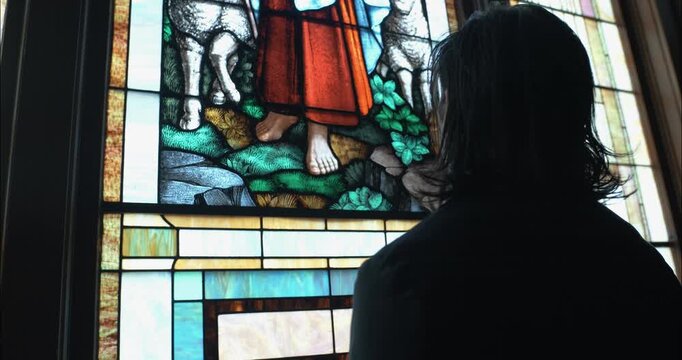 Dramatic shot of a man in silhouette looking at stained-glass art inside a church sanctuary, conveying a cinematic, moody, and contemplative atmosphere.