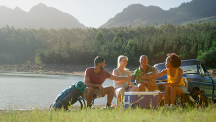 Group Of Friends With Backpacks By Pick Up Truck On Road Trip Drinking Beer From Cooler By Lake