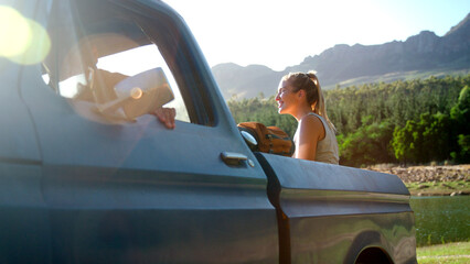 Woman Sitting In Back Of Pick Up Truck On Road Trip By Lake At Sunset