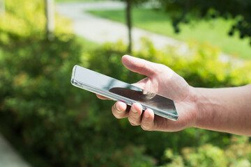 Close-up of a hand holding a smartphone outdoors on a sunny day.