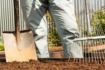 man standing in garden with shovel and rake, ready for work