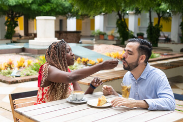 Interracial couple sharing cake and coffee at outdoor cafe