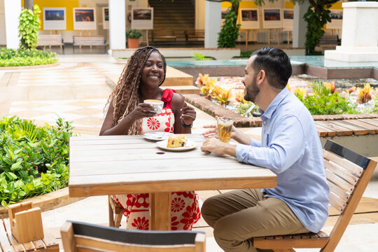 Cheerful multi-ethnic couple enjoying coffee and cake at outdoor cafe