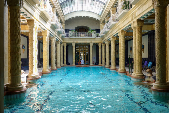 View of turquoise water shimmers under the glass roof, reflecting ornate columns and balconies in the Gell&Atilde;&copy;rt Thermal Bath, Budapest, Hungary.