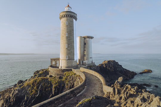 View of the Minou lighthouse with a red top standing tall on a rocky outcrop surrounded by the sea, connected by a stone path, Plouzan&Atilde;&copy;, France.