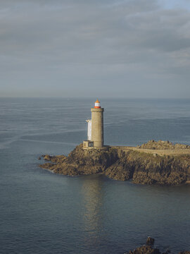 View of the Petit Minou lighthouse standing guard atop rugged cliffs where the land meets the sea, under a sky heavy with clouds, Plouzan&Atilde;&copy;, France.
