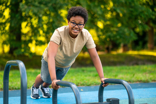 Curly-haired teen exercising at the playground and looking excited - Powered by Adobe
