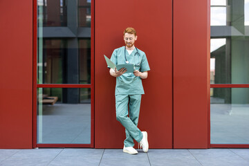 Male clinician with red hair checking open medical files outside
