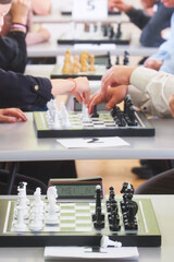 Row of chess boards in play at a club event  anonymous hands make opening moves while clocks tick, selective focus on the nearest game, vertical frame. Photo © slexp880