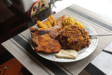 A top view of a plate of delicious Gallo pinto and pork chop with plantain, scrambled egg, and...