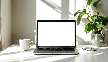 Fototapeta premium Bright and modern home office desk with a blank laptop screen for mockup, a coffee cup, and a green plant in a sunlit room