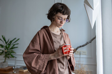 Stressed, disappointed woman standing alone at home with cup drink, upset reflecting on life....
