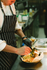 chef is pouring pasta into a bowl of french fries on the kitchen table