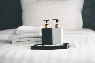 bottles of bathroom accessories on white cleaned bed in hotel bedroom, in soft focus
