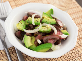 salad of black tomatoes, avocado and onions in white ceramic bowl
