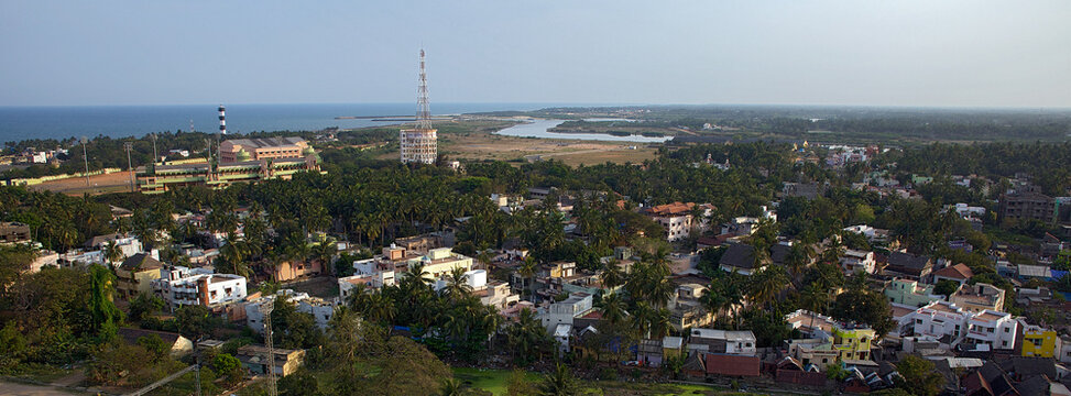 Aerial view of buildings nestled amid lush greenery and a winding river meeting the ocean, punctuated by a tall tower, Puducherry, Puducherry, India.