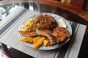 A top view of a plate of delicious Gallo pinto and pork chop with plantain, scrambled egg, and...
