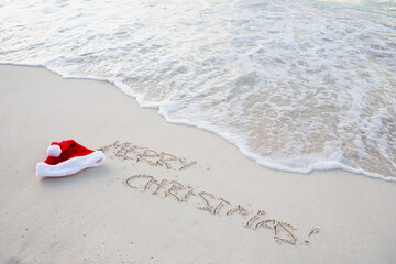 Santa hat and Christmas greetings written in beach sand