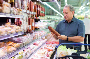 Elderly man chooses sausage in supermarket