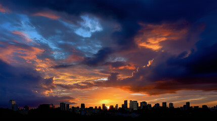 Fototapeta premium Dramatic sunset behind city skyline, buildings in dark silhouette with glowing clouds.