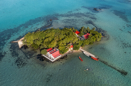 Aerial view of the island Mouchoir rouge, a verdant islet dotted with red-roofed structures, embraced by the shimmering turquoise waters of the lagoon, Mahebourg, Grand Port District, Mauritius.