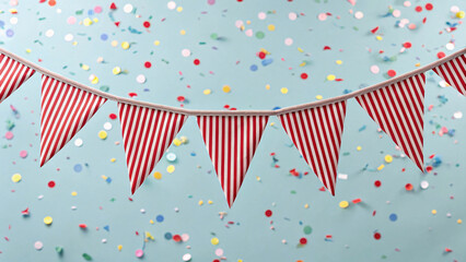 Red and white striped carnival bunting banner against soft blue background with colorful confetti...
