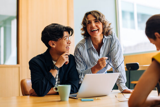 Professionals engaged in lively discussion around a laptop during a meeting