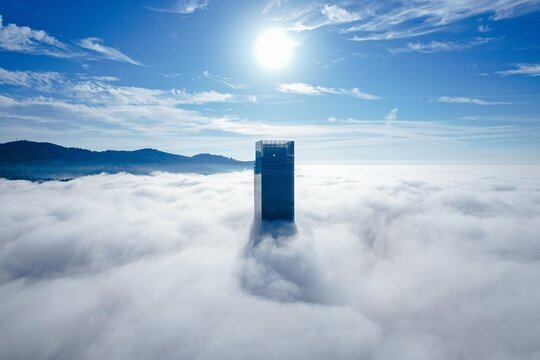 Aerial view of a skyscraper piercing through a sea of fluffy white clouds under a bright sun, Palazzo della Regione Piemonte, Piemonte, Italy.