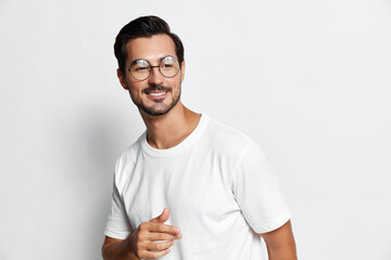 Smiling man wearing glasses and a white t-shirt poses confidently while pointing with his finger,...